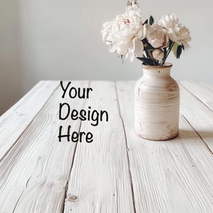 May include: White ceramic vase with a rustic finish, filled with white peonies and greenery, sitting on a whitewashed wood table. The text "Your Design Here" is written on the table.
