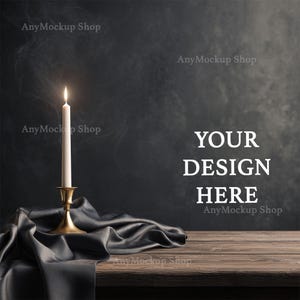 以下が含まれることがあります： 木製のテーブルの上に、金色の燭台に立てられた白いろうそくが燃えています。濃い灰色のサテンの布がテーブルに置かれています。「YOUR DESIGN HERE」のテキストが濃い灰色の背景に表示されています。