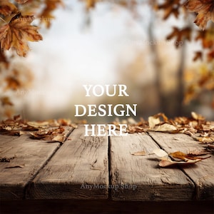 May include: A rustic wooden table covered in fallen autumn leaves, with the text "YOUR DESIGN HERE" in white. The background is blurred, showing a soft, out-of-focus view of a forest with warm, autumnal colors.