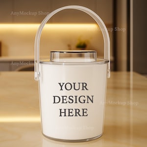 Può includere: Un secchiello per il ghiaccio bianco con manico e coperchio trasparenti. Il testo "YOUR DESIGN HERE" è stampato sulla parte anteriore del secchiello. Il secchiello è su una superficie marrone chiaro.