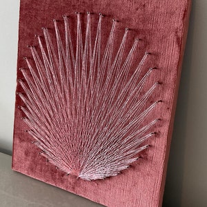May include: A pink velvet canvas with a white string art design in the shape of a fan.