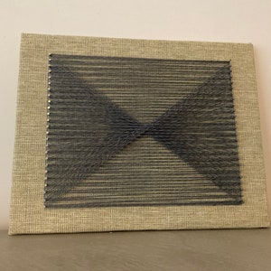 May include: A black string art piece with a geometric design on a beige canvas.