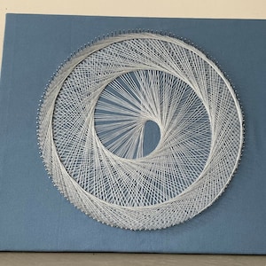 May include: A white string art design of a spiral on a blue canvas.