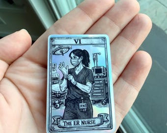 May include: A rectangular holographic sticker designed like a tarot card featuring a black and white illustration of a nurse in scrubs and a face mask putting on gloves in a hospital room with the text VI and THE ER NURSE printed on the card.