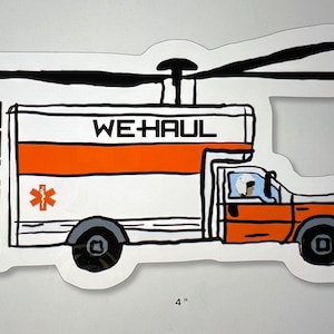 May include: A white and orange cartoon truck with a helicopter on top. The truck has the words "WE HAUL" written on the side. The truck is 4 inches wide and 2.4 inches tall. The truck has a red star of life symbol on the side. The truck has a cartoon driver in the cab.