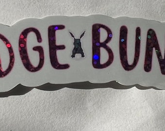 May include: A white sticker with a pink glittery design that says "Badge Bunny" with a small black bunny silhouette in the middle.