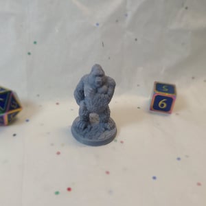 Op de afbeelding: Een grijs 3D-geprint miniatuur van een gorilla die op een basis staat. De gorilla staat in een verdedigende houding met zijn armen gekruist voor zijn borst.