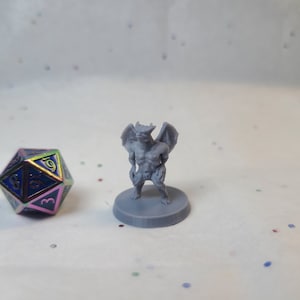 Puede incluir: Una miniatura de gárgola gris impresa en 3D con alas, de pie sobre una base redonda. La miniatura mide aproximadamente 5 cm de alto.