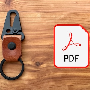 May include: A black carabiner keyring with a brown leather strap and a black key ring. A red and white PDF icon is on the right. The items are on a wooden surface.