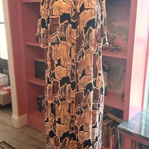 May include: A button-down dress with a unique pattern featuring tan, black, and brown geometric shapes and animal prints. The dress has short sleeves and a round neckline. The dress is displayed on a mannequin.