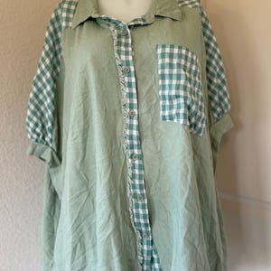 May include: A light green button-down shirt with short sleeves. The shirt features a gingham pattern on the sleeves, pocket, and collar. The front placket and hem have a frayed edge.