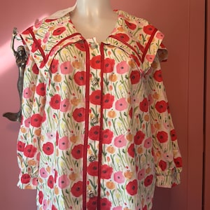 May include: A long-sleeved button-down shirt featuring a white base with a vibrant floral print of red, pink, and orange poppies and green stems. The shirt includes a wide sailor-style collar with red trim and decorative silver-toned buttons.