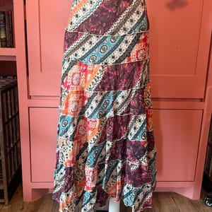 May include: A tiered maxi skirt featuring a vibrant patchwork design with diagonal bands of paisley, floral, and geometric patterns in shades of deep burgundy, bright orange, turquoise, and white, finished with a comfortable elasticized waistband.