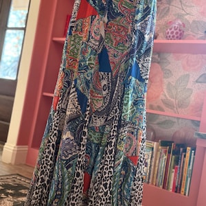 May include: A long, flowing skirt with a patchwork design featuring paisley, floral, and geometric patterns in shades of blue, red, green, and orange. The bottom of the skirt has a leopard print border. The skirt appears to be made of a lightweight fabric.