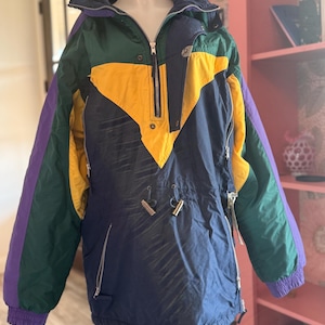 May include: A vintage anorak-style jacket in a color block design. The jacket features a navy blue base with yellow, green, and purple accents. It has a zippered front, a drawstring hem, and zippered pockets. The jacket is displayed on a mannequin.