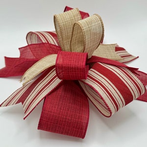 May include: A red and cream striped ribbon bow with a cream burlap ribbon bow on top. The bow is tied with a knot in the centre.