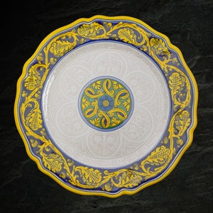 May include: A white ceramic plate with a blue and yellow floral design. The plate has a scalloped edge and a raised center.