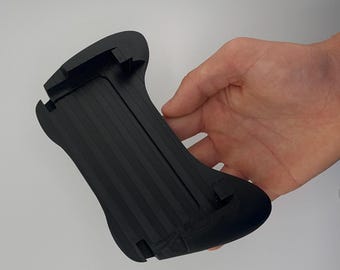 Peut inclure: Une poignée de manette de jeu portable noire présentant une forme ergonomique profilée avec un canal central encastré et des poignées latérales texturées. L'appareil a une finition mate solide et comprend des fentes intégrées sur les bords.