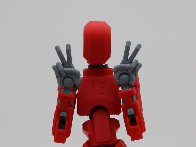 May include: A red and gray robot toy with articulated arms and legs. The robot is making a peace sign with both hands.