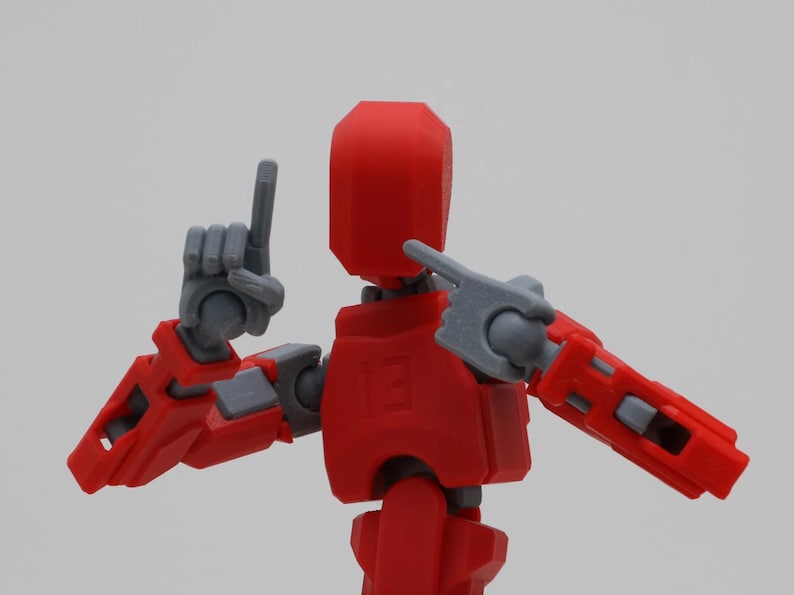 May include: A red and gray articulated robot toy with posable arms and legs. The robot has a red head and a gray body. The robot is in a pose with its arms raised and its legs spread apart.