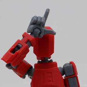 May include: Red and gray articulated robot toy with a hand raised in the air. The robot has a red body and gray arms and legs.