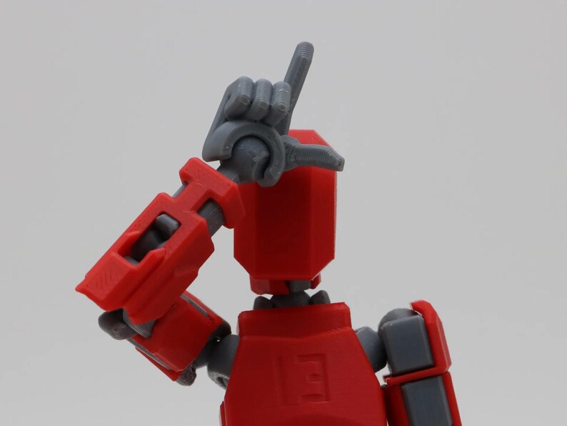 May include: Red and gray articulated robot toy with a hand raised in the air. The robot has a red body and gray arms and legs.