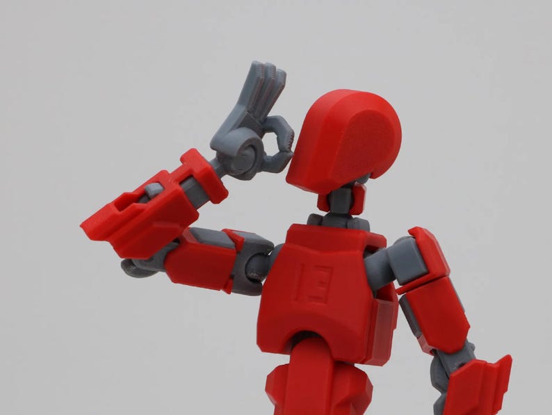 May include: A red and gray articulated action figure with a raised arm and hand. The figure has a red head and torso, and gray arms and legs.