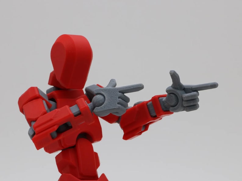 May include: A red and gray articulated action figure with posable arms and legs. The figure is pointing with both hands.