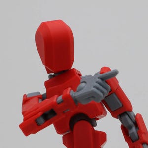 May include: A red and gray articulated action figure with a rounded head and a pointing finger.