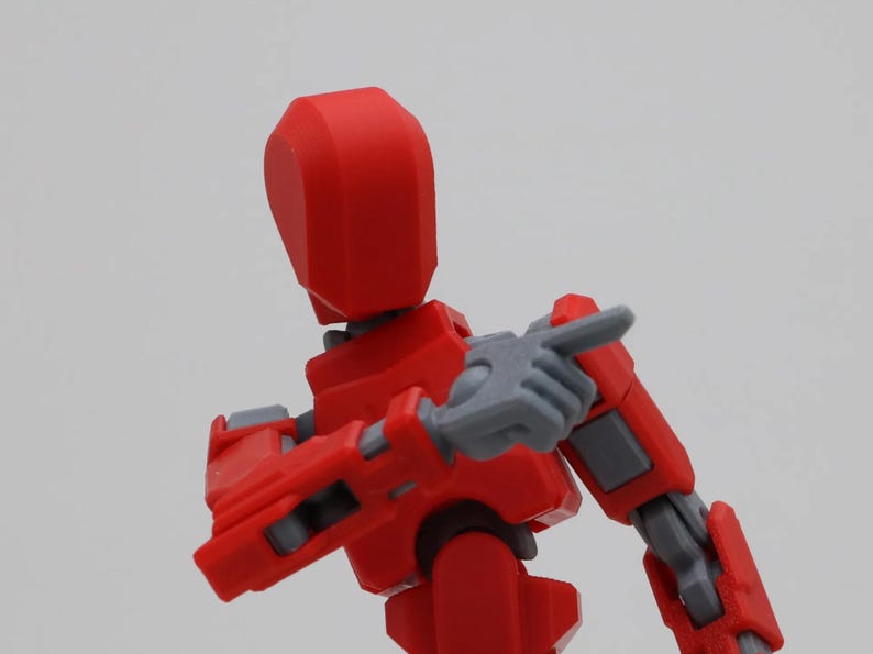 May include: A red and gray articulated action figure with a rounded head and a pointing finger.