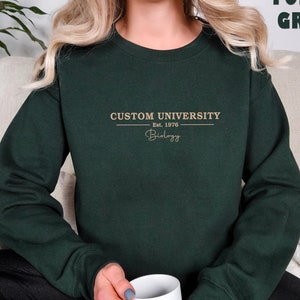 May include: A dark green sweatshirt with the text "CUSTOM UNIVERSITY Est. 1978 Biology" printed in gold on the front.