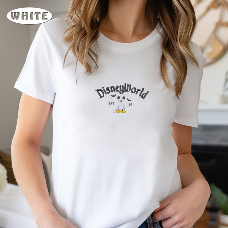May include: White t-shirt with a DisneyWorld graphic. The graphic features the text "DisneyWorld" above a ghost-like Mickey Mouse character, with "EST. 1971" below. The design includes bats and Mickey Mouse's yellow shoes.