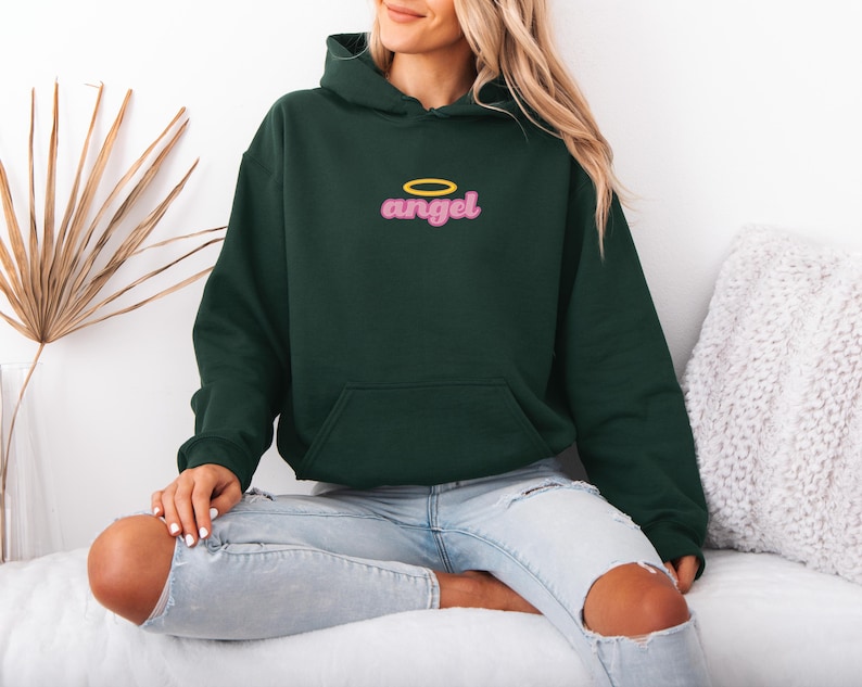 May include: Dark green hoodie with a front pocket and a hood. The word "angel" is embroidered in pink with a yellow halo above it. The hoodie is made of a soft material.