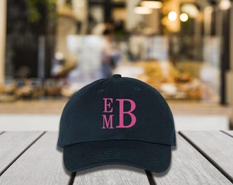 May include: A dark blue baseball cap with a pink embroidered monogram "E M B" on the front.