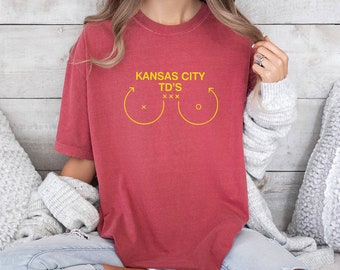 May include: A red t-shirt with the text "Kansas City TD's" and a graphic of two yellow circles with arrows pointing upwards.