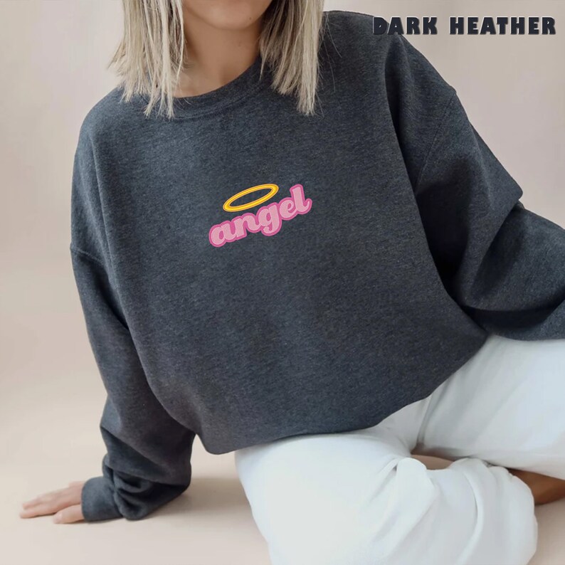 Puede incluir: Una sudadera gris oscuro jaspeada con un gr&aacute;fico rosa de estilo retro "angel" con un halo amarillo sobre la palabra.