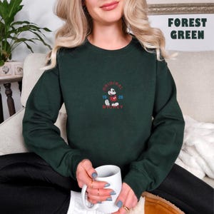 May include: A forest green long-sleeve sweatshirt featuring an embroidered graphic of Mickey Mouse in the center. The text reads ORIGINAL MICKEY 19 28 in red and blue thread. The sweatshirt has a crew neckline and ribbed cuffs and hem.