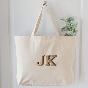 May include: A beige canvas tote bag with the letters "JK" embroidered in brown on the front.