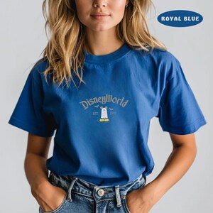 May include: Royal blue t-shirt with the text "DisneyWorld" in a stylized font. Below the text is a graphic of a ghost wearing Mickey Mouse's shoes. The shirt also has the text "EST. 1971".