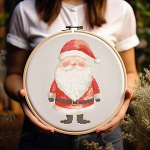 Puede incluir: Un aro de bordado de punto de cruz con fondo blanco y un diseño de Papá Noel rojo y blanco. Papá Noel lleva un traje rojo con ribete blanco y una barba blanca.