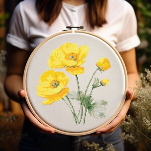 May include: A close-up of a hand-stitched embroidery hoop with a floral design. The hoop features a white background with yellow flowers and green leaves.