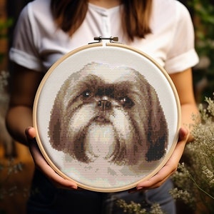 Op de afbeelding: Een close-up van een kruissteekborduursel van een Shih Tzu hond in een houten borduurring. De hond is bruin en wit en heeft een serieuze uitdrukking.