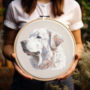 Puede incluir: Una bordado de punto de cruz blanco y marrón de la cabeza de un perro en un aro de bordado de madera.