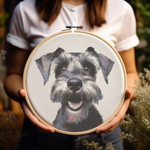 Peut inclure: Un cerceau de broderie en point de croix avec un motif de chien miniature schnauzer gris et blanc. Le chien sourit et a un nez noir.