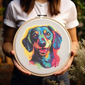 May include: A colourful cross-stitch embroidery of a dachshund dog's head in a wooden embroidery hoop. The dog's fur is a mix of blue, green, yellow, and pink.