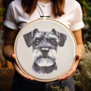 Könnte beinhalten: Eine Kreuzstich-Stickerei des Gesichts eines Schnauzer-Hundes, präsentiert in einem Holzreifen. Das Fell des Hundes ist in Grau-, Schwarz- und Weißtönen mit detaillierten Stichen dargestellt. Der Hintergrund ist ein neutraler Stoff.