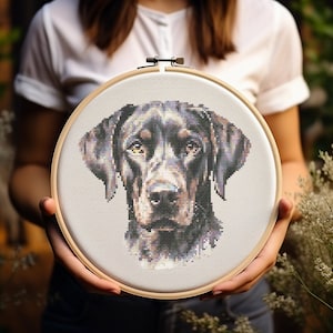 May include: A cross-stitch embroidery hoop with a black and brown dog's head design. The dog has a serious expression and is looking directly at the viewer.