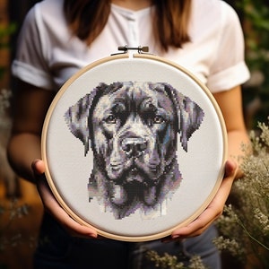May include: A cross-stitch embroidery of a dog's face, with a detailed pixelated design in black, grey, and purple. The artwork is stretched within a round wooden embroidery hoop. The dog's portrait is centered on the white fabric.