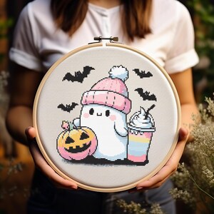 May include: A white ghost wearing a pink and white hat, holding a pink and yellow pumpkin and a pink and white milkshake. The ghost is surrounded by black bats on a light grey background.