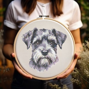 May include: A cross-stitch embroidery hoop featuring a detailed image of a grey and white miniature schnauzer dog. The dog's face is the focus of the image, with its eyes, nose, and whiskers clearly visible.